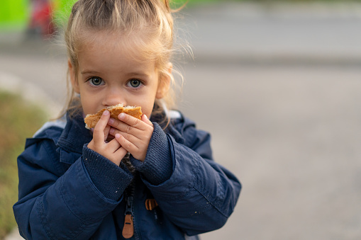 Una hermosa niña caucásica con el pelo rubio y comer pan con ansiosamente con sus manos mira a la cámara con ojos tristes photo