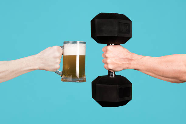 men are holding out each other a glass of beer and a large dumbbell - healthy drink imagens e fotografias de stock