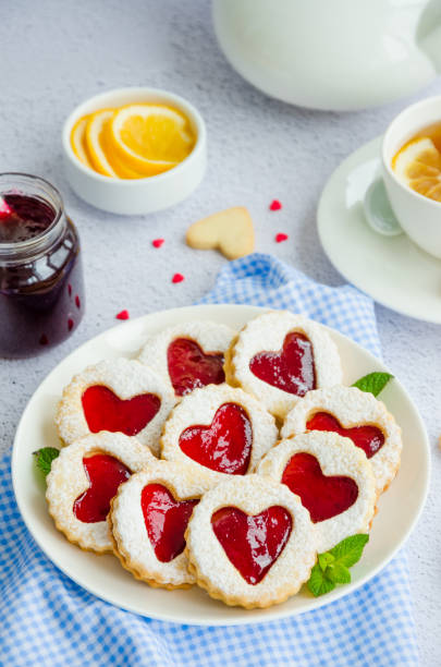 istock Linzer cookies with heart with raspberry jam and powdered sugar on a white plate with a cup of tea. Dessert on Valentine's Day. Vertical orientation 1203619030