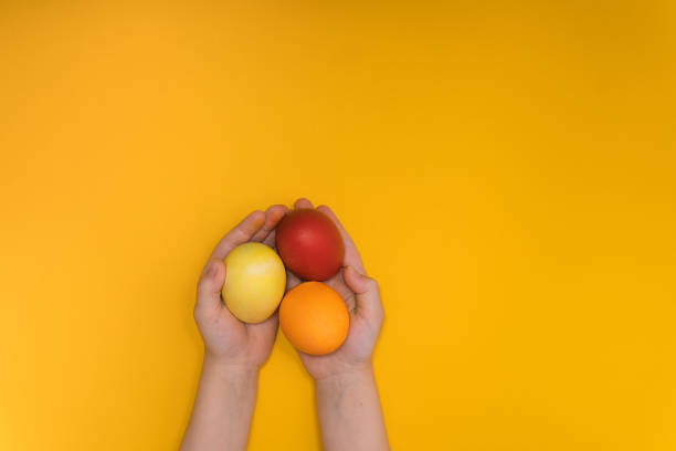 istock children hands hold chicken egg decorated. Handmade Easter design. Yellow background 1203627656