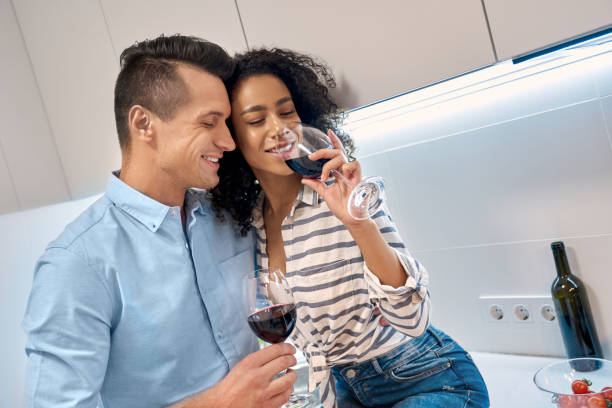 istock Romantic Date. Young multiethnic couple standing at kitchen cooking dinner hugging drinking wine smiling delightful 1203642342
