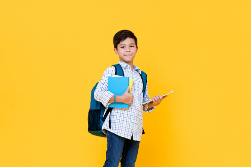 Handsome schoolboy with backpack holding books and tablet computer