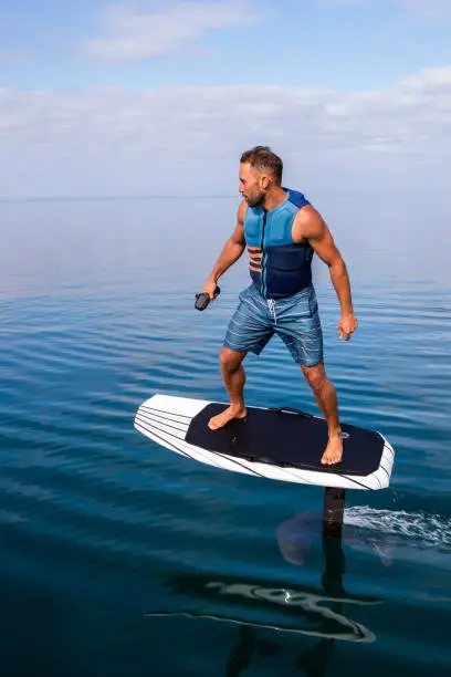 Man riding an electric hydrofoil foil board on a lake with a life jacket