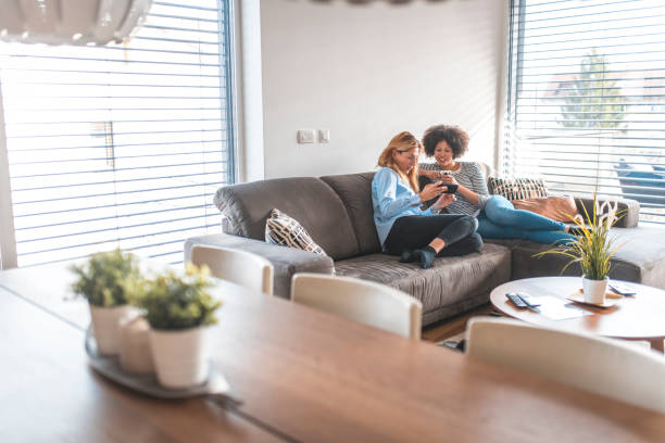 istock Woman sharing phone with friend sitting on sofa 1203655287