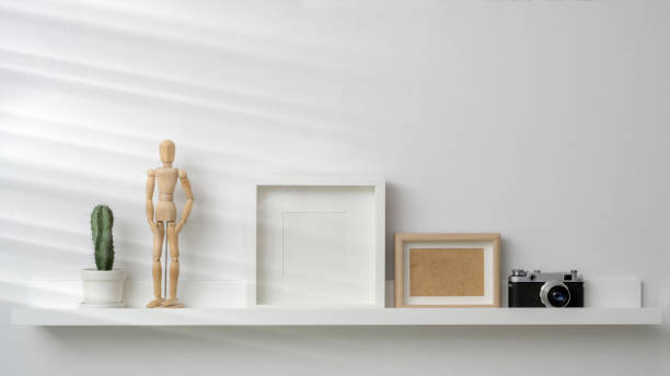 istock Cropped shot of mock up frames, camera and decorations on white shelf with white wall background 1203666329