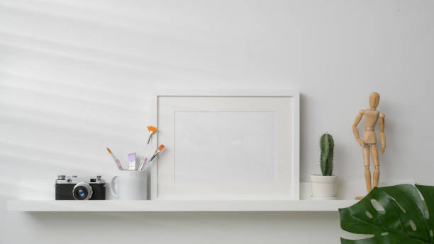 istock Close up view of mock up frame, camera and decorations on white shelf with white wall background 1203666952