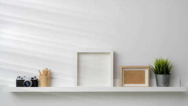 istock Close up view of mock up frames, camera and decorations on white shelf with white wall background 1203667021