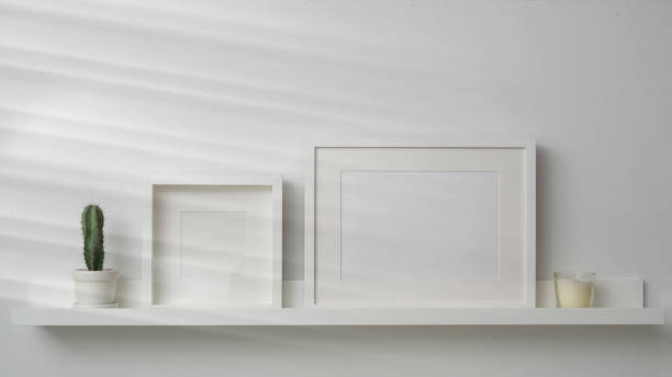 istock Close up view of mock up frames and decorations on white shelf with white wall background 1203667027