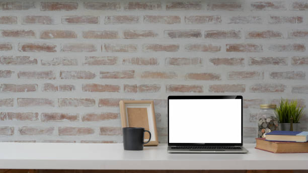 istock Cropped shot of blank screen laptop, mock up frame and decorations on white table with brick wall background 1203667074