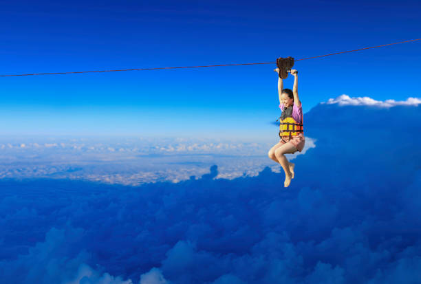 Exciting adventure activity. young girl hanging on a rope-way ride on the Zipline on blue sky background. stock photo