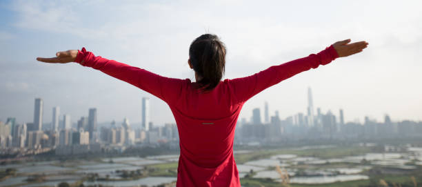 istock Cheering female open arms on mountains next to modern city 1203672812