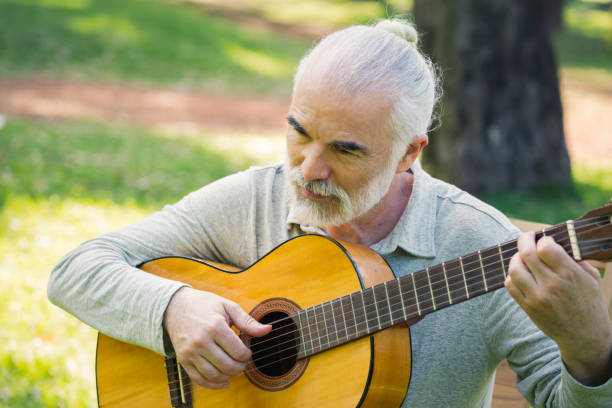 istock Senior man playing acoustic guitar in the park 1203677215