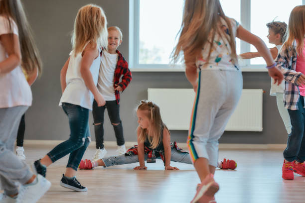istock Gymnastic exercises. Little cute girl sitting on a twine while having a choreography class. Group of positive and active children learning a modern dance in the dance school 1203678505