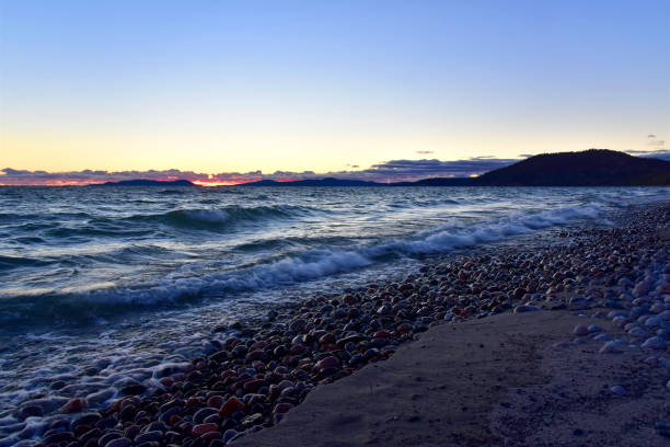 The autumn sun sets on a dark and brooding wavy Lake Superior beach, Marathon, Ontario, Canada