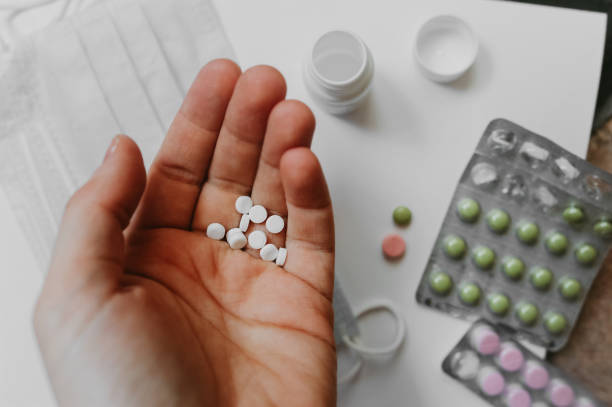 istock in the light-skinned hand of a human, handful small white tablets against a background of blurred medical items, colored tablets in the package and respiratory masks 1203679476