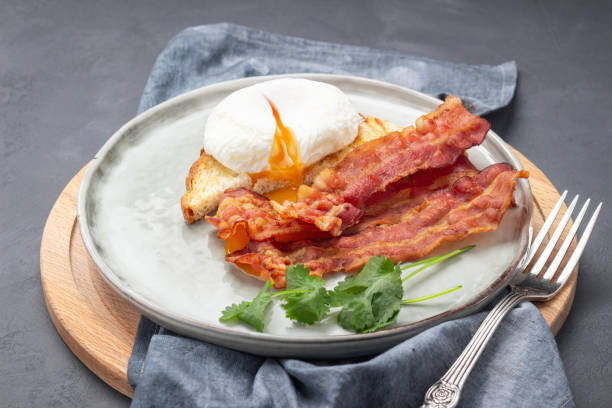 istock Fried bacon pieces and poached eggs on a plate. 1203680368