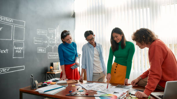 istock Creative people. Professional team of young web designers working on a new project together and discussing ideas while standing in the modern and bright office 1203682114