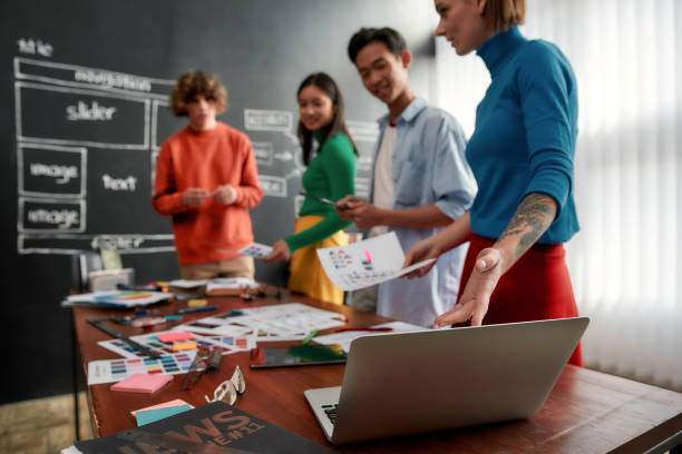 istock Perfect colour palette. Group of four web designers in casual wear developing new web site layout and looking at color swatches while having a meeting in the modern office. Web design concept 1203685372