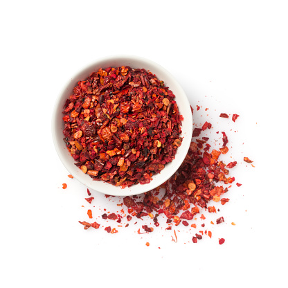 Top view of dried hot red pepper flakes in bowl for spicy food isolated on white background