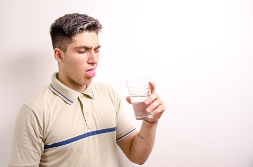 young Caucasian man looking disgustedly at a glass of water in his hand, white background