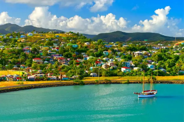 Colourful image of a single sailboat moored in St John`s Harbour, Antigua with colourful Caribbean homes on the surrounding hills.