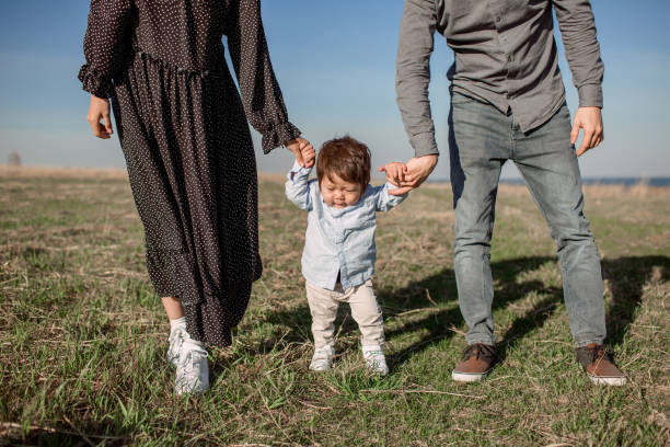 istock Cute Asian Boy Makes His First Steps Holding His Parents Hands In Simmer Field 1203689039