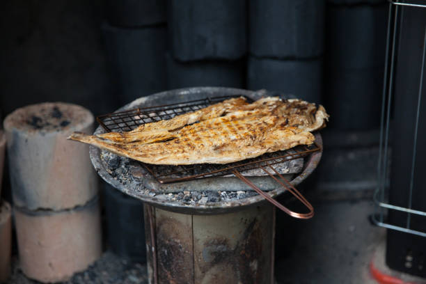 Fish being grileld on a charcoal fire on a small wire rack. Korean traditional dried fish on a grill.