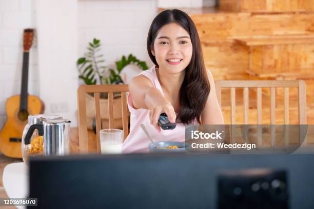 Asian Woman Wathcing Tv On Demand And Use Remote Control Change Television Channel At Breakfast In Morning Stock Photo - Download Image Now