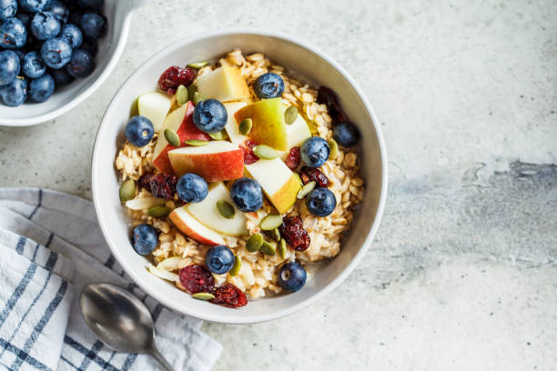 bircher muesli o farina d'avena notturna con mela, banana e mirtilli in ciotola grigia, vista dall'alto. - oat wheat oatmeal cereal plant foto e immagini stock