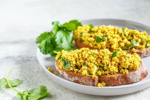 Tofu scramble with greens toast on a gray plate. Healthy vegan food concept.