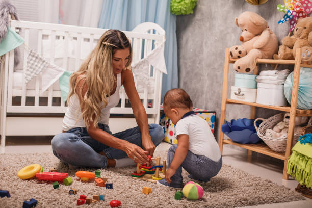 Traditional toys for development of motor skills Front view of baby sitter and toddler bonding and playing with wooden toys on the carpet of kid's room. baby squatting stock pictures, royalty-free photos & images