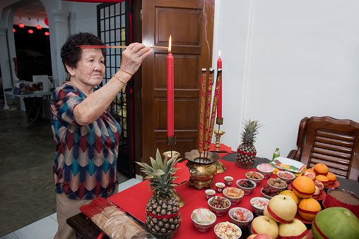 Elderly woman lighting up joss sticks and perform thanksgiving offering to the Jade Emperor at the 8th night of Chinese Lunar New Year.