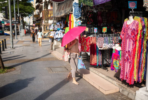 Georgetown, Malaysia - February 25, 2018: A woman protects herself from the sun with an umbrella while shopping for clothes.