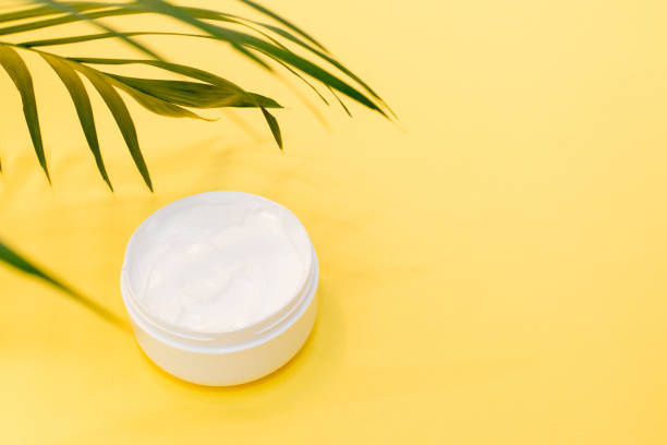 istock Face cream with spring greenery on yellow background with a copy space 1203704016