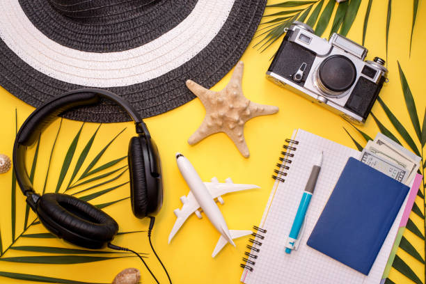 istock Flat lay top view with hat, pen, headphone, camera, notebook and green leaf for travel concept on soft yellow background. 1203704127