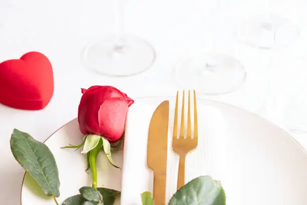 Red rose on white plate with gold cutlery and heart shape  box . Saint valentines day celebration or propose romantic dinner concept.
