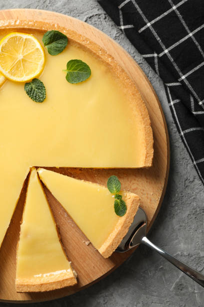 istock Wood board with lemon tart on grey background with towel, top view 1203706304