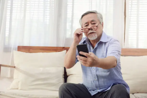 Older men move glasses down to look at the phone in the hand due to long sighted problems, which makes vision difficult.Health problems of the elderly.
