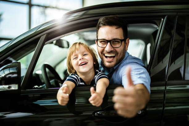 This car is perfect for us! Happy single father and son testing new car in a showroom and showing thumbs up. car ownership photos stock pictures, royalty-free photos & images