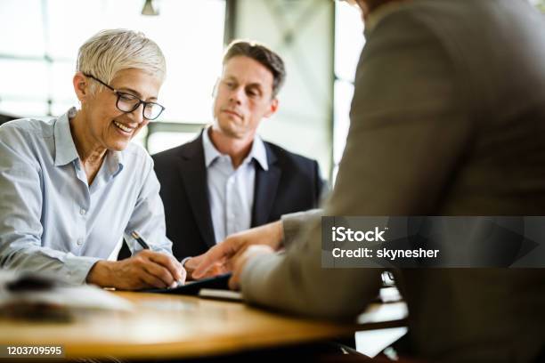 Happy Business Couple Signing A Contract On A Meeting With Their Agent Stock Photo - Download Image Now