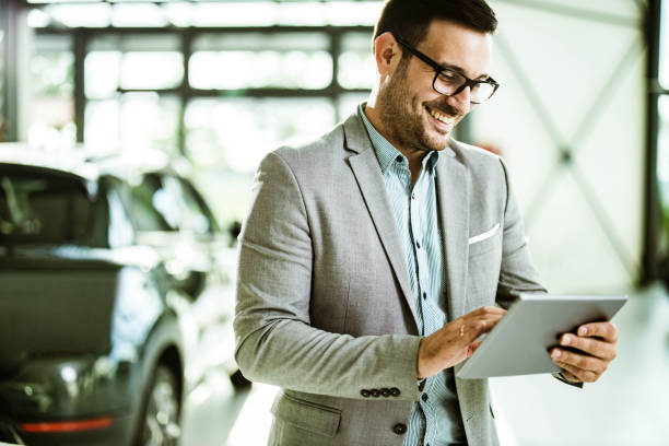 Happy salesman with digital tablet in car showroom. Young happy car salesperson reading an e-mail on digital tablet in showroom. car salesperson photos stock pictures, royalty-free photos & images