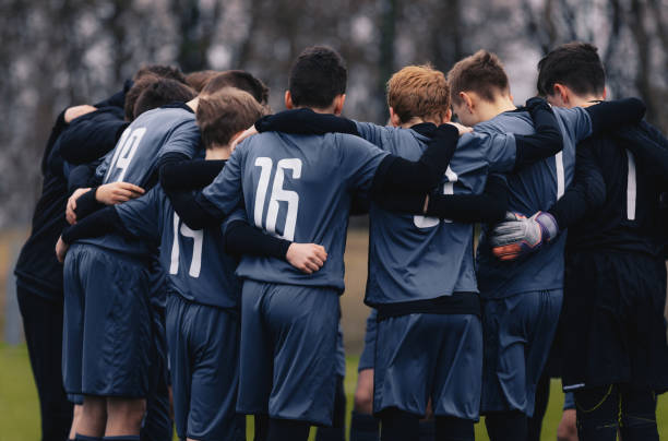 time de futebol com treinador júnior se reunindo em um círculo, para estratégias e motivação. time juvenil de futebol se destaca em gramado - futebol de clubes - fotografias e filmes do acervo