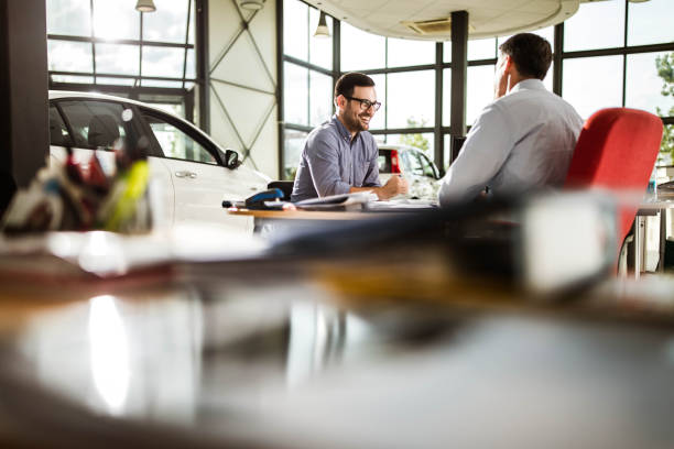 Young happy man talking to car salesperson in a showroom. Happy male customer communicating with salesman during a meeting in a car showroom. car salesperson photos stock pictures, royalty-free photos & images