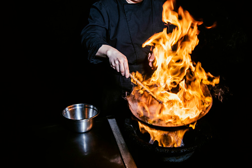 Skilled male chef lights the wok on fire.