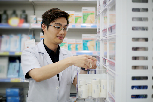 A male adult pharmacist is taking out surgical tape from shelves in pharmacy.