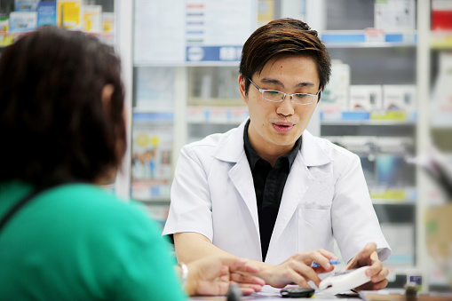 A male adult pharmacist is accessing his patient's medical history while she's on blood pressure test in pharmacy.