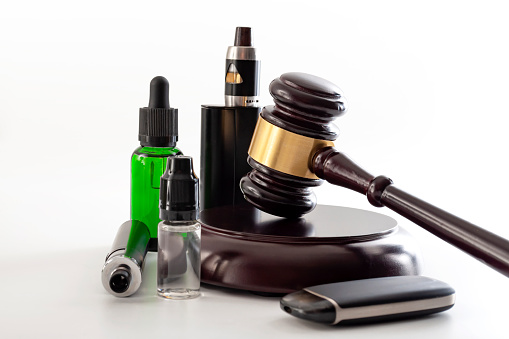 Legal act to restrict vaping, outlaw smoking electronic cigarettes and vape ban legislation conceptual idea with judge gavel, vape device and bottle of ejuice isolated on white background