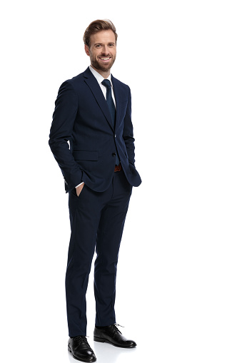 happy young businessman holding hands in pockets and smiling, standing isolated on white background, full body
