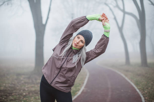 Exercising woman at foggy day Gray hair women exercise outdoor in park, she is stretching after running. She is wearing sports clothing. Fogy and cold weather one mature woman only stock pictures, royalty-free photos & images