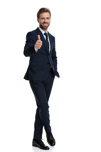 happy young businessman smiling and making thumbs up sign, standing isolated on white background, full body